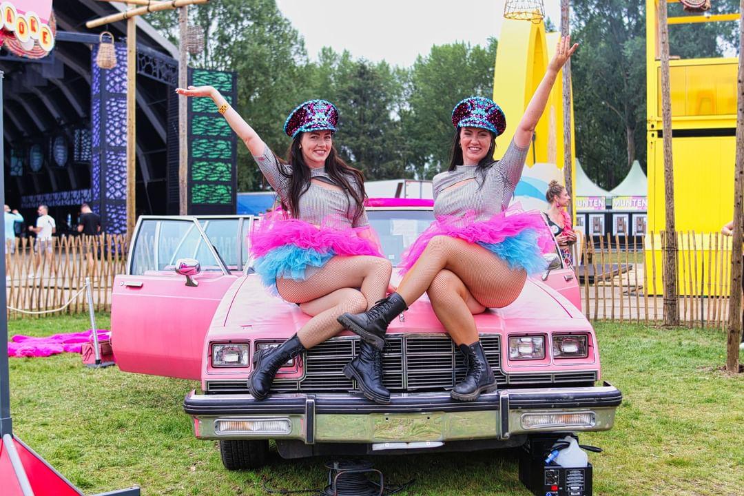 Polaroid Ladies poseren op een roze cadillac op het festivalterrein