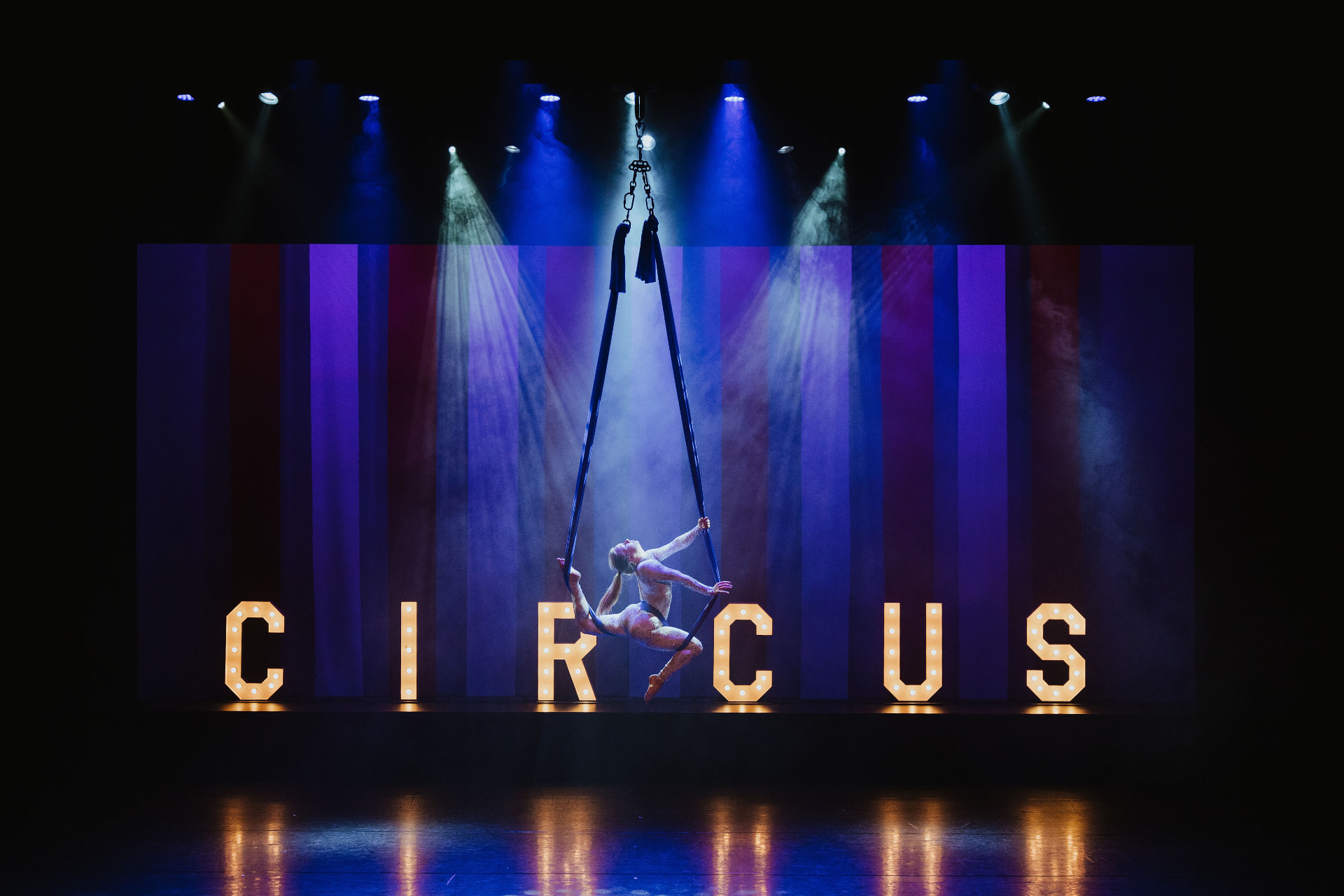 Aerial act aan het doek boven een podium met lichtgevende CIRCUS-letters