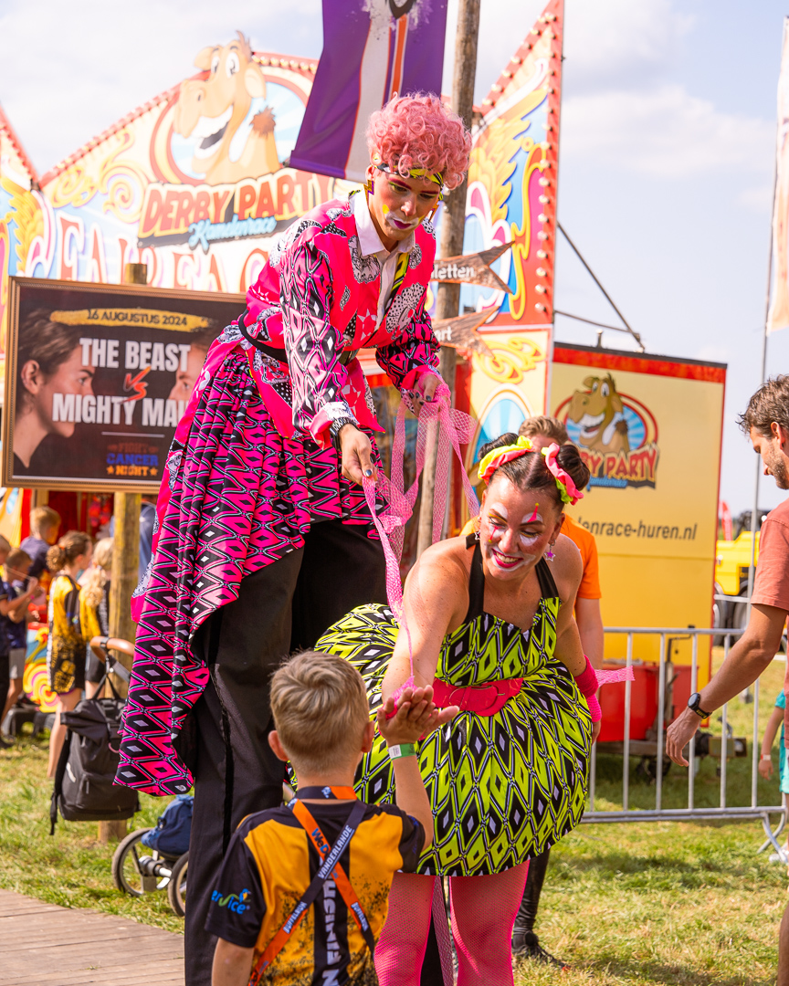 Poppenspeler act op stelten maakt contact met een jonge bezoeker op de kermis