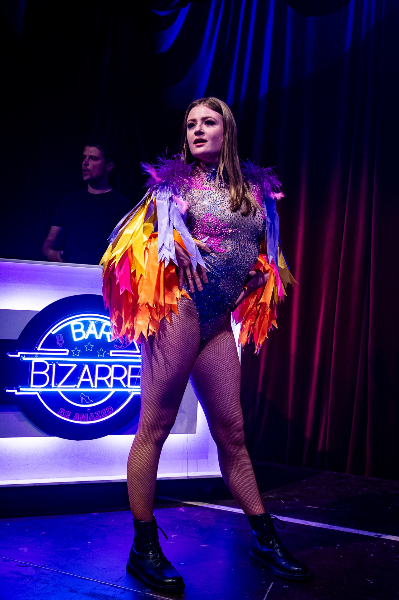 Zangeres in glitterpak met kleurrijke verenmantel op het podium