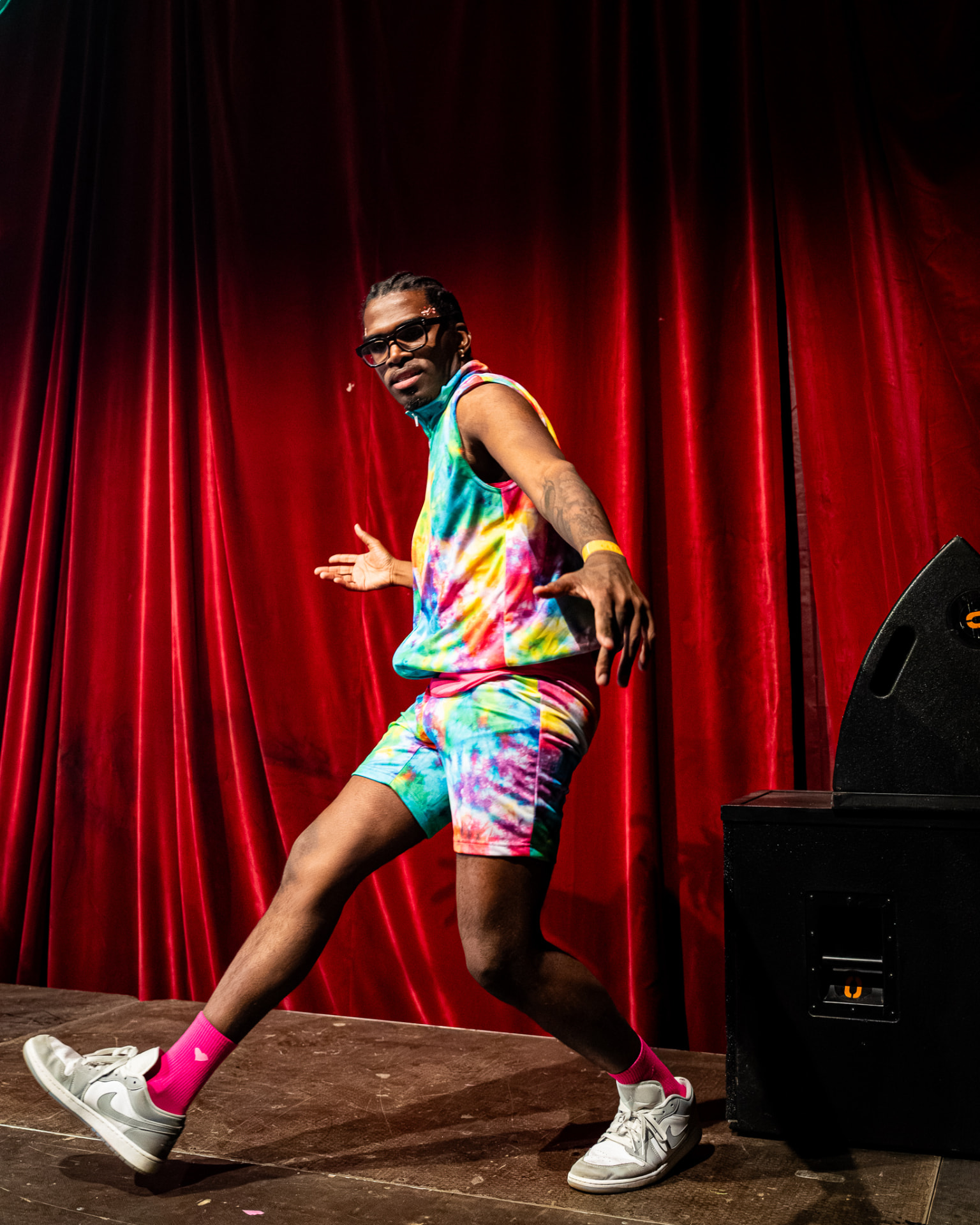 Danser in tie-dye outfit poseert voor een rood theatergordijn