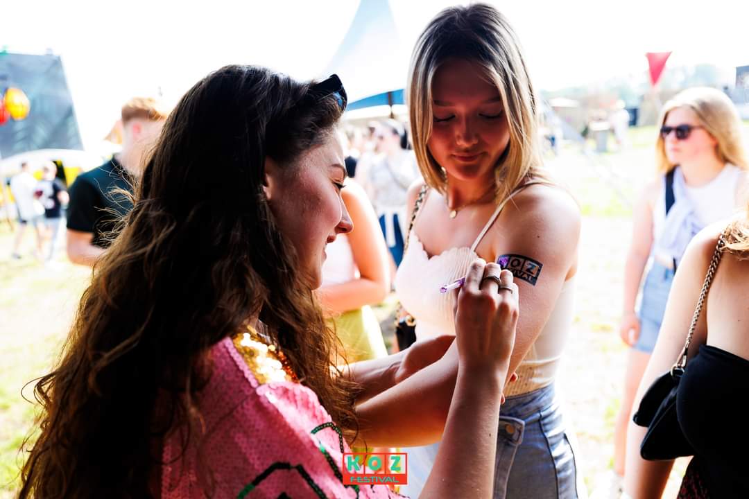 Glitter tattoo met festivallogo wordt op de schouder van een gast gezet
