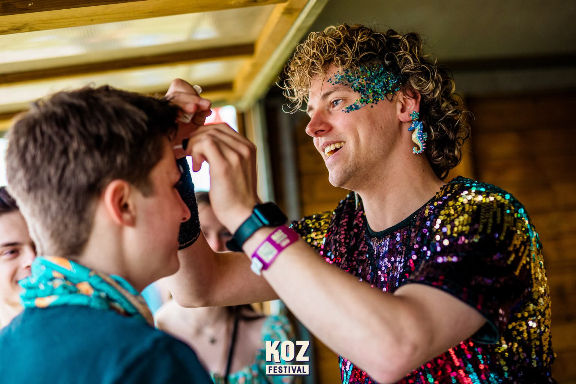 Glitter artist in pailletten shirt brengt festival glitters aan op het gezicht van een bezoeker