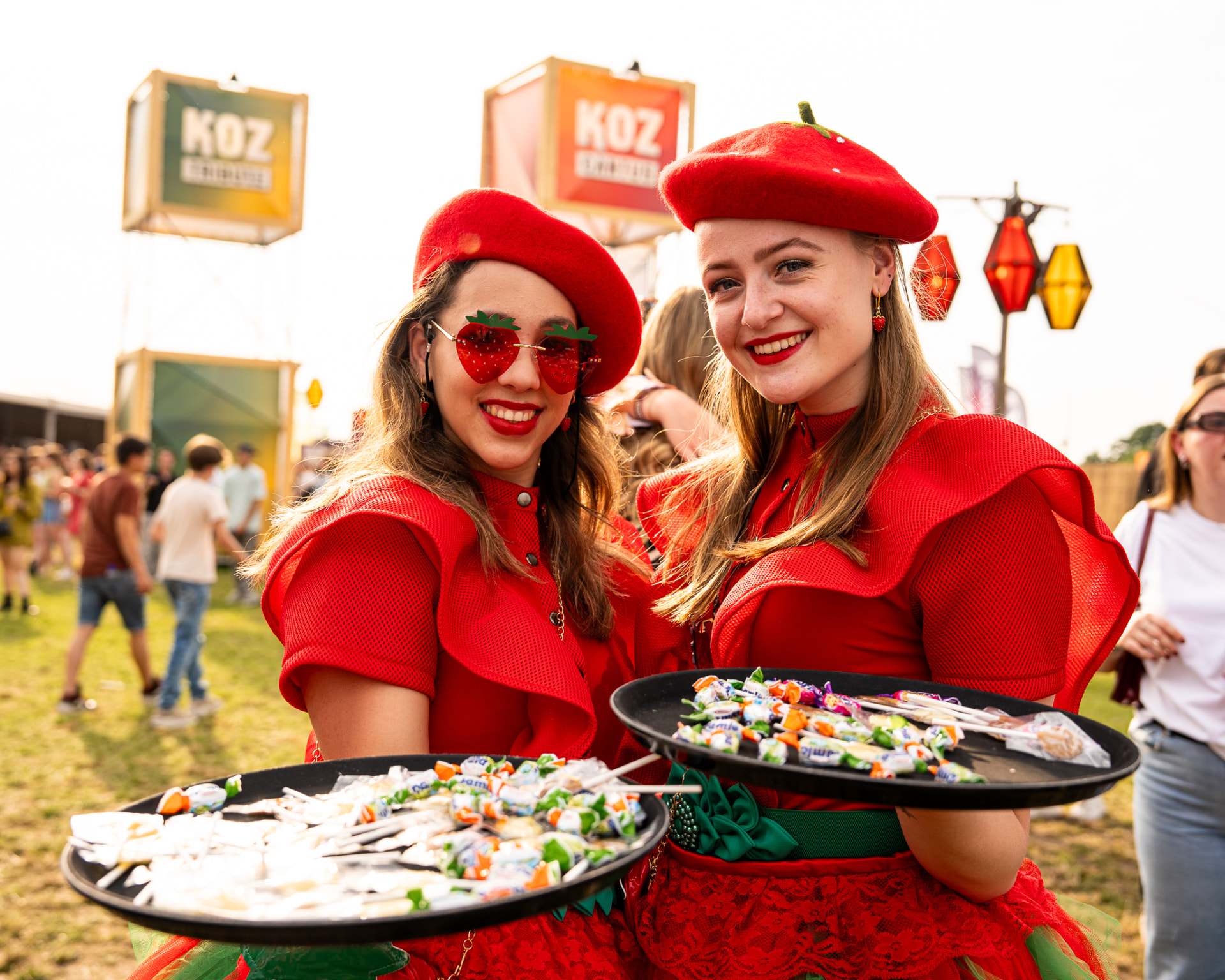 Twee hostessen in rode aardbeienoutfits met snoepschalen op Koz Festival